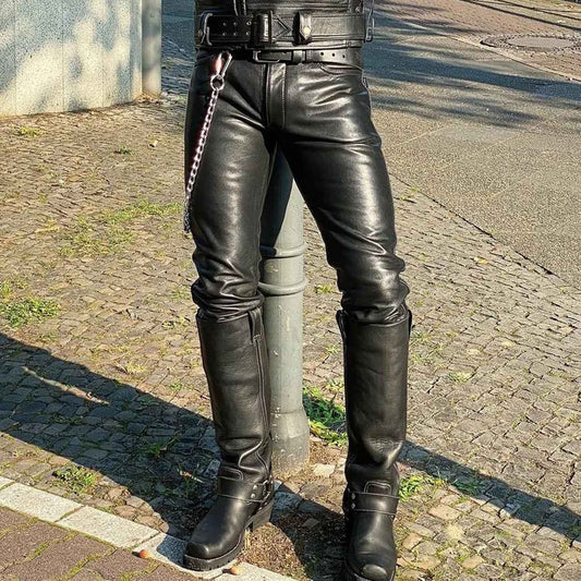 Black leather pants worn by a person standing outdoors on a cobblestone street, paired with tall black leather boots and a black belt with a chain detail.