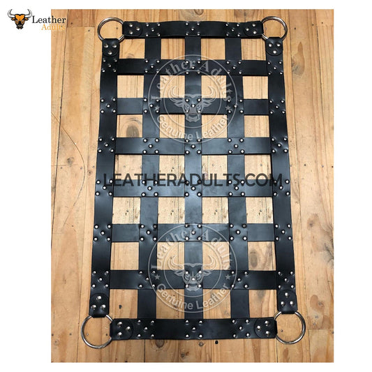 A black leather cargo swing sling with stirrups, featuring a grid-like pattern and branded with the text 'LEATHERADULTS.COM'.