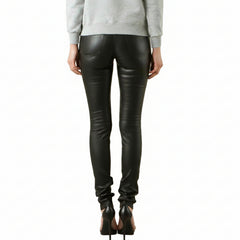 Rear view of a model wearing black lambs leather skinny jeans with a gray graphic print on the left leg, paired with a light gray sweatshirt and black high heels, against a white background.
