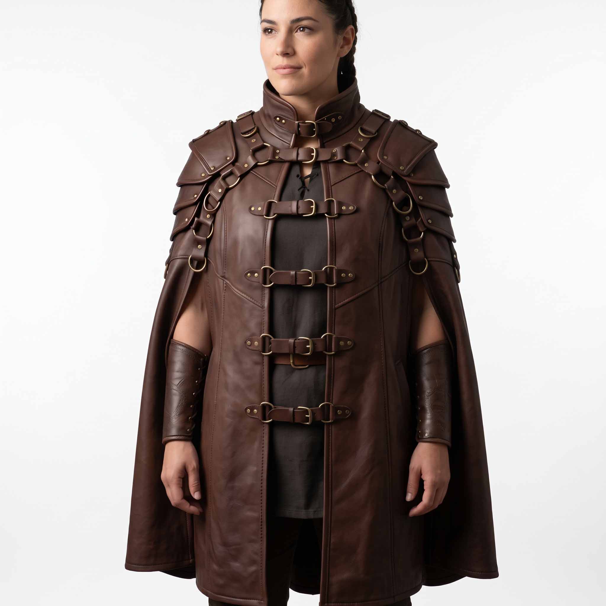Front view of woman wearing handmade brown cowhide leather medieval cloak with tiered shoulder pauldrons, roller buckles, and matching leather bracers