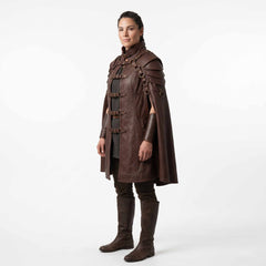 Side three quarter view of woman wearing tailored brown leather viking cape with tiered armor pauldrons and matching leather gauntlets