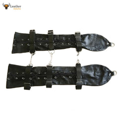 This image shows a pair of black leather arm restraints, designed for adults. Each restraint features multiple straps with buckles for adjustability, as well as lacing details along the length. Metal D-rings or similar attachments are visible at the ends and along the sides, suggesting they can be connected or secured. The overall appearance is robust and functional.