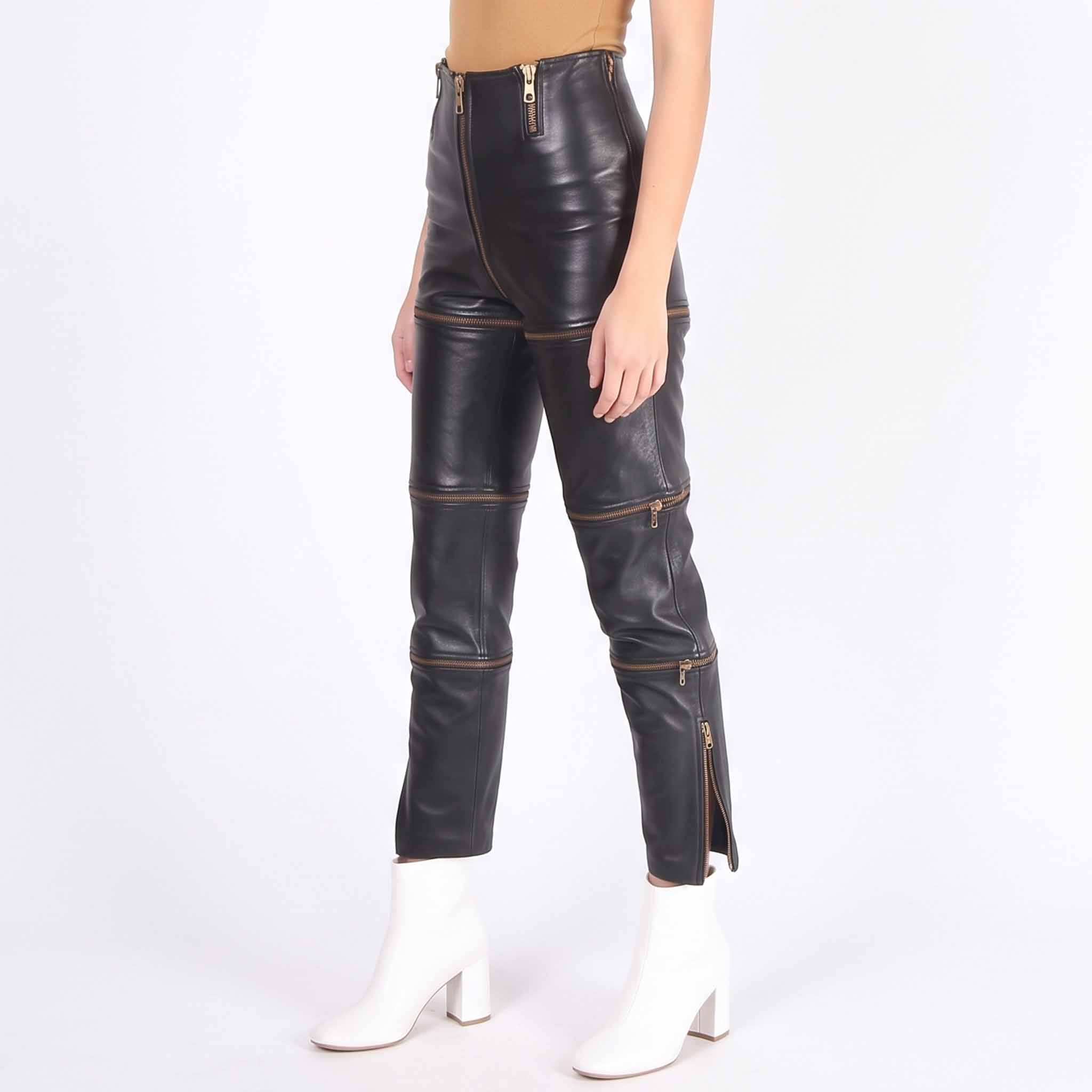 Front three quarter view of woman wearing high waisted black leather convertible pants with gold horizontal zip off panels paired with white boots