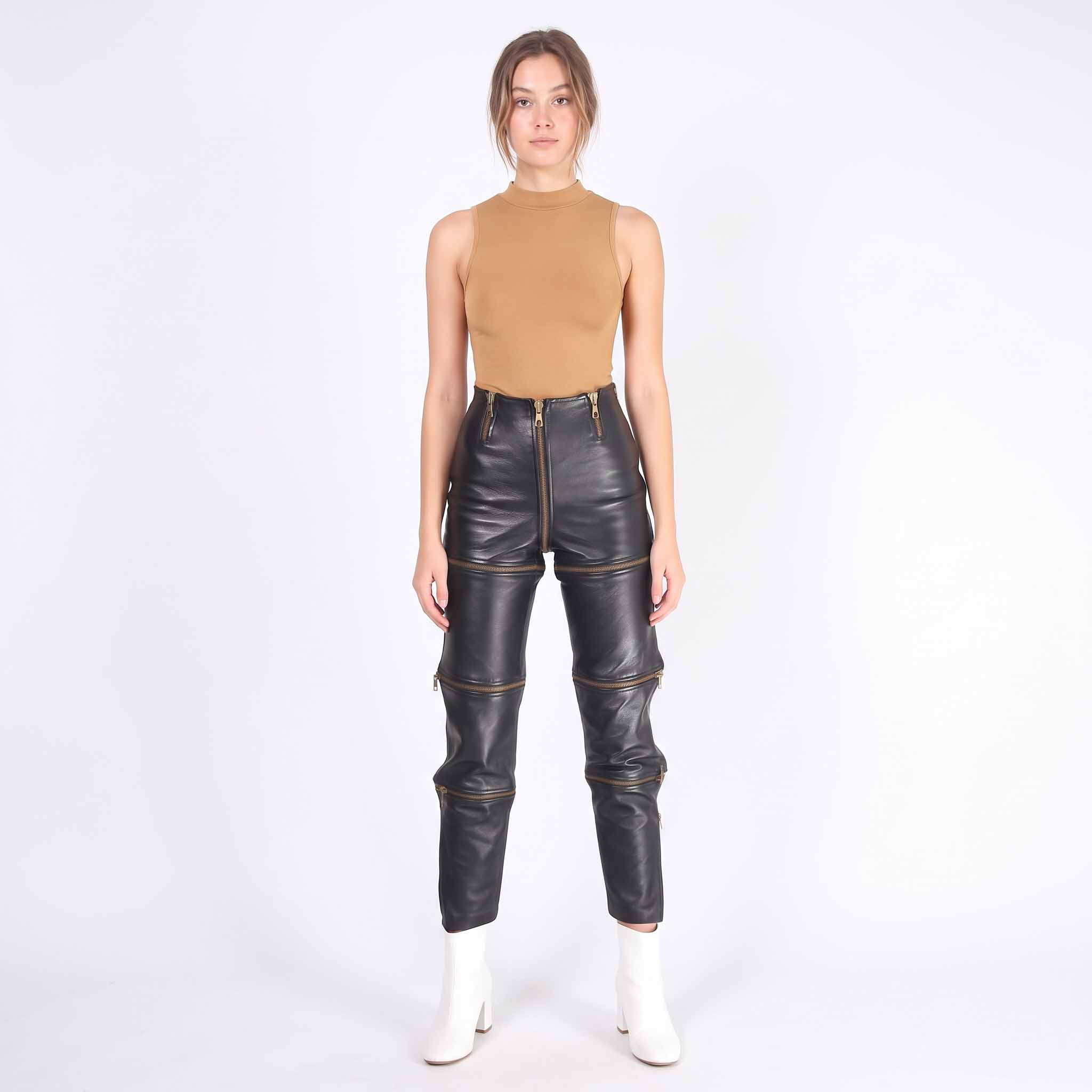 Full length front studio portrait of woman modeling high waisted black leather convertible trousers with white ankle boots