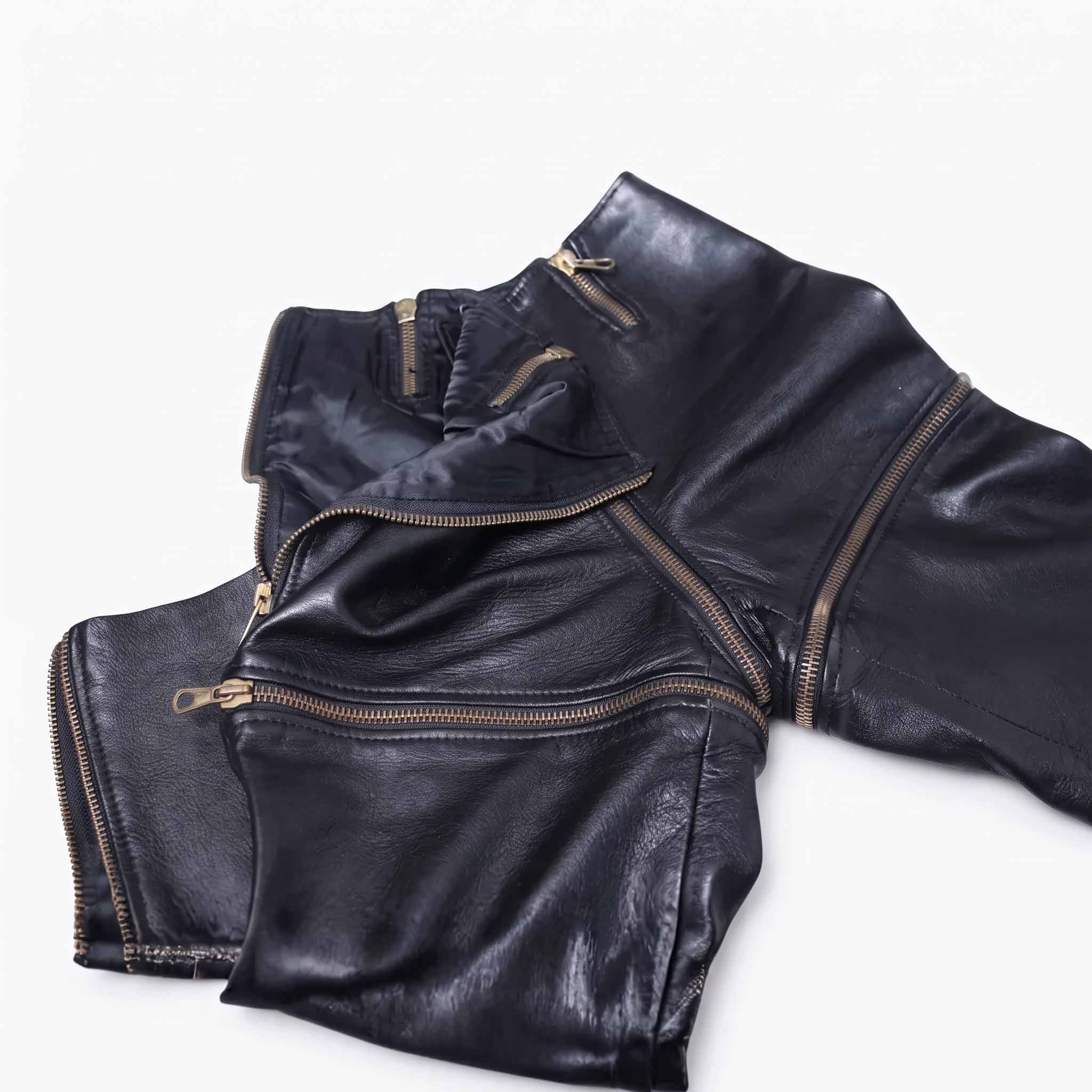 Close up flat lay detail of black leather zip off trousers displaying antique gold metal teeth, zipper pulls, and satin lining