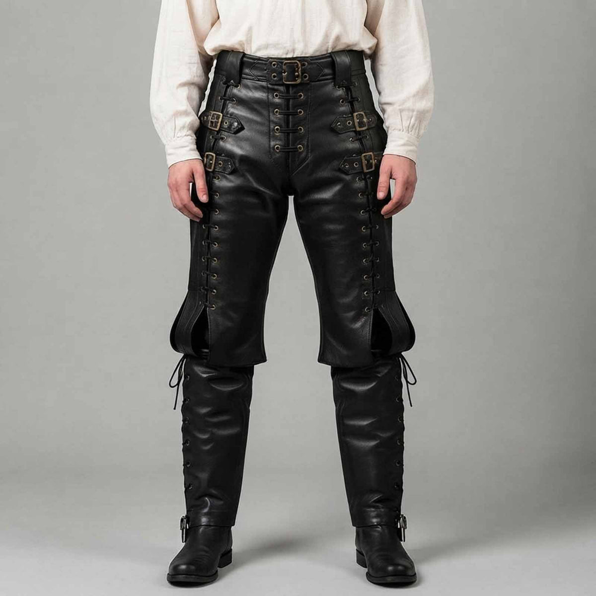 Front studio view of a man wearing black real leather Renaissance pants with side lacing, waist buckles, and attached boot covers against a neutral grey backdrop.