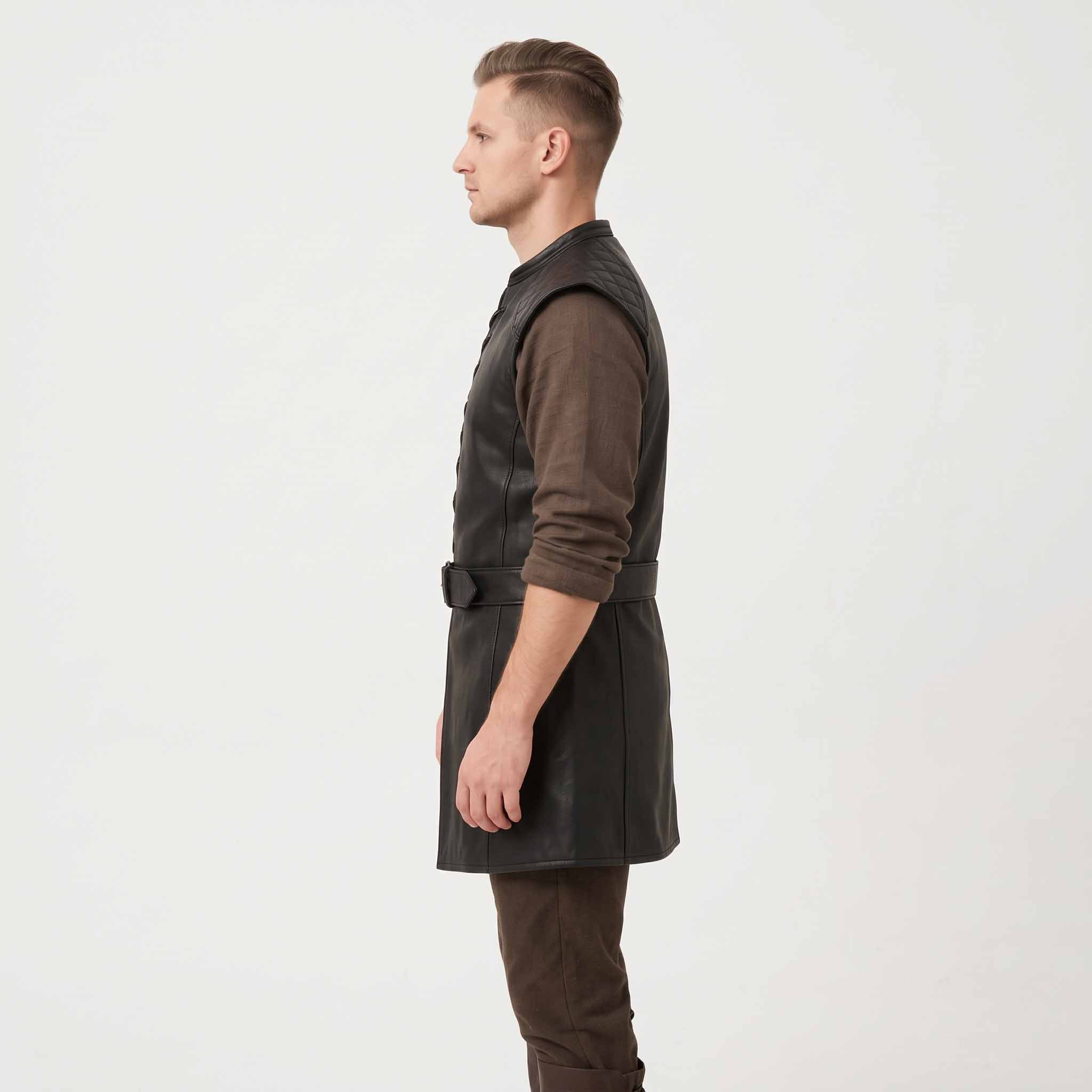 Side profile studio shot of man wearing longline black leather medieval tunic showing armhole cut, belted waist, and side length