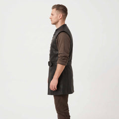 Side profile studio shot of man wearing longline black leather medieval tunic showing armhole cut, belted waist, and side length