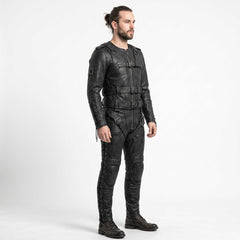 Side profile shot of bearded man wearing tailored black leather restraint suit showing bicep D rings, ribbed knee pads, and lace up pant legs