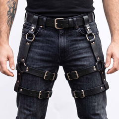 Front view of man wearing handmade black cowhide leather thigh harness with double roller buckle leg straps over black washed denim jeans