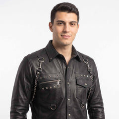 Close up view of mens black leather shirt highlighting point collar, silver pyramid studs, metal eyelets, chest pockets, and curb link chains