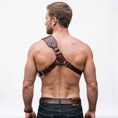 Direct rear view of muscular man showcasing back strap architecture of brown leather shoulder harness with rear tension buckle