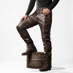 Man posing with one foot on rustic barrel wearing brown leather steampunk strap pants highlighting criss-cross thigh straps and roller buckles