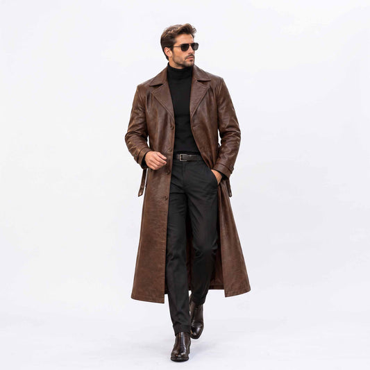 Full length front view of handsome man walking in handmade brown genuine leather long trench coat open over dark turtleneck and trousers