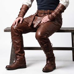 Man seated on wooden bench wearing brown genuine leather warrior pants and arm bracers showing relaxed drop crotch drape and calf buckle straps