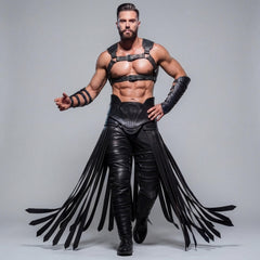 Front view of athletic warrior model posing in black cowhide leather chest harness, armored forearm bracers, and dramatic leather fringe girdle