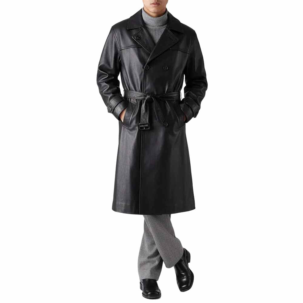 Full body view of a man wearing a black real cowhide leather double-breasted trench coat tied at the waist with grey trousers.