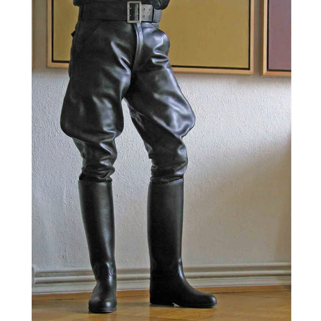 Black leather riding breeches with a black belt, worn with matching tall black leather riding boots, shown on a model standing on a metal stool in an indoor setting.
