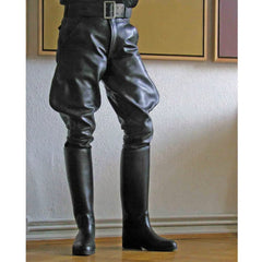 Black leather riding breeches with a black belt, worn with matching tall black leather riding boots, shown on a model standing on a metal stool in an indoor setting.