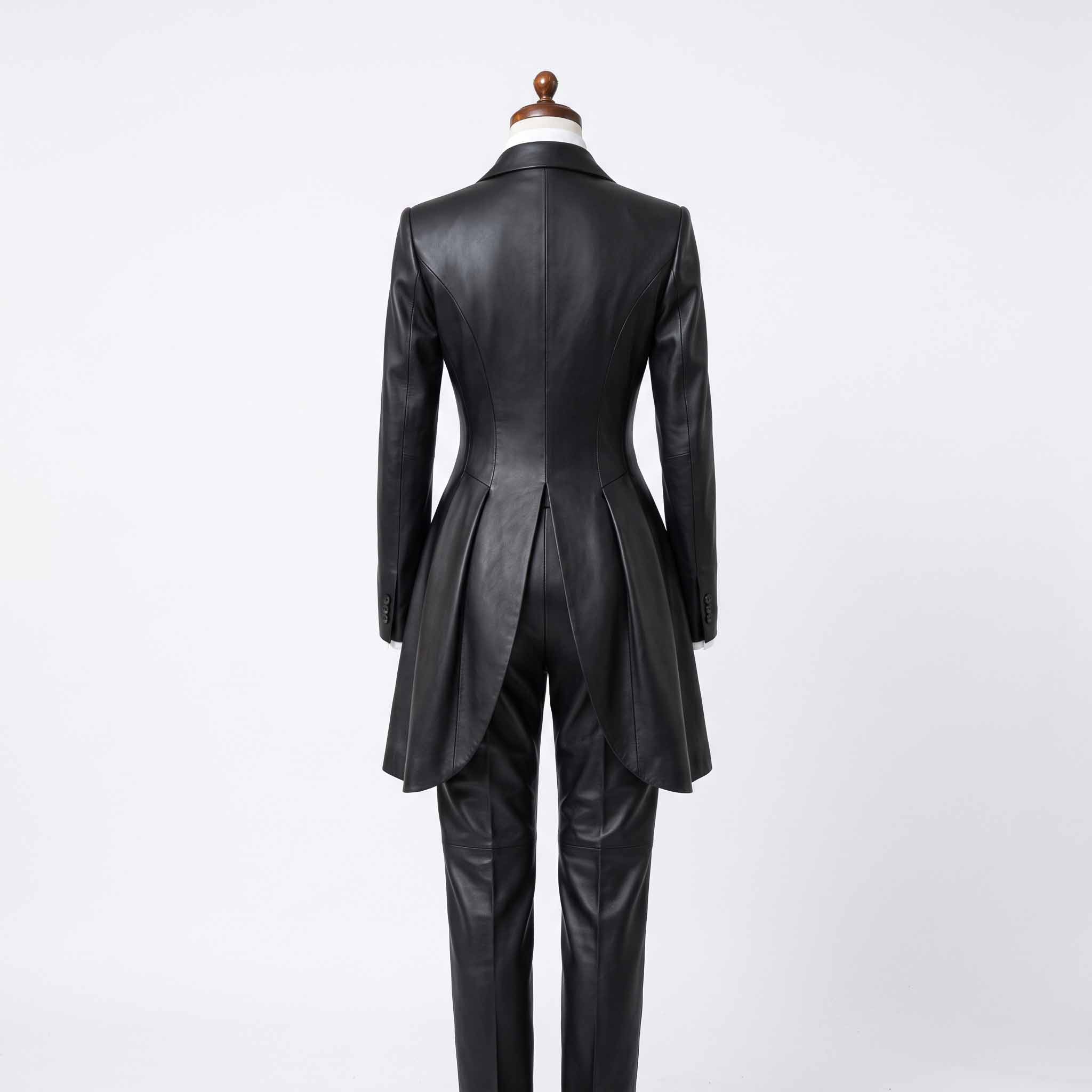 Rear full length view of womens handmade black leather swallowtail coat and straight leg trousers on mannequin stand on white background