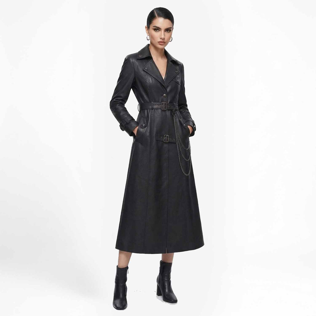 Front view of a woman wearing a long black leather trench coat with a belted waist and hanging chain detail, paired with heeled boots.