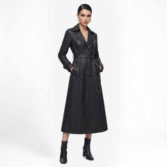 Front view of a woman wearing a long black leather trench coat with a belted waist and hanging chain detail, paired with heeled boots.