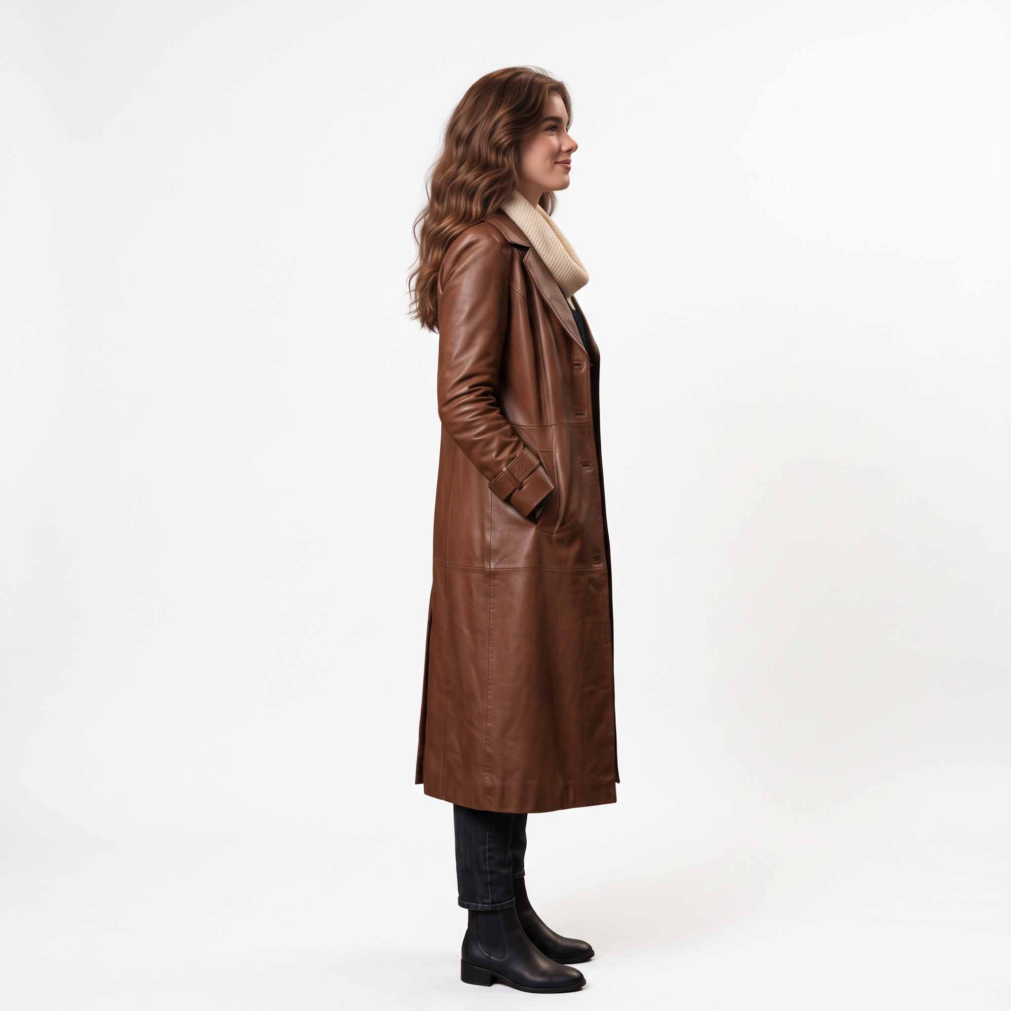 Side profile angle of woman wearing long brown leather duster overcoat showing tailored sleeve cuff tabs and hands in side pockets