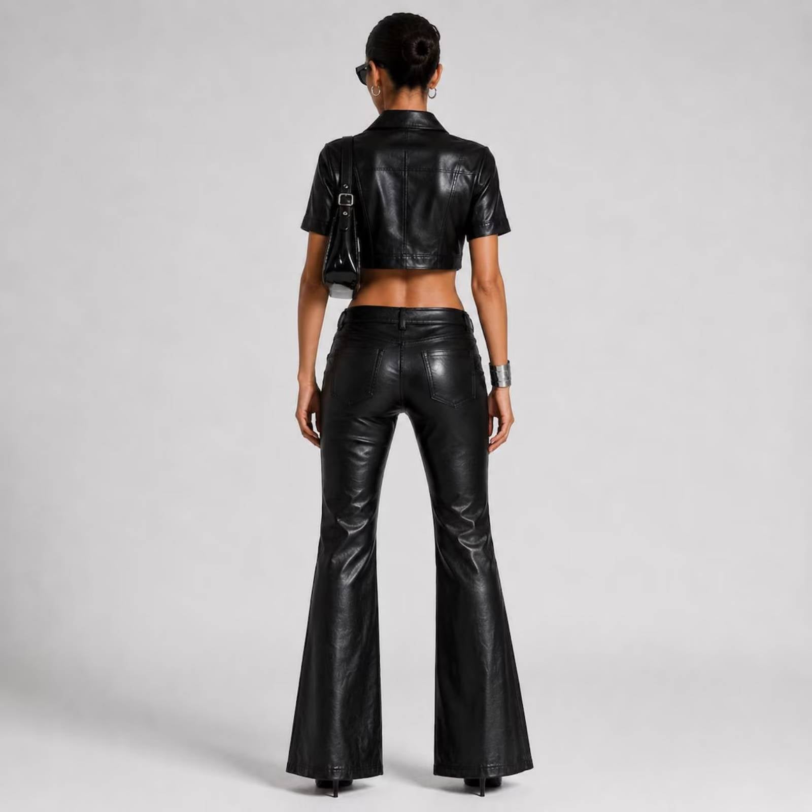 Back view showing the rear yoke detailing on the leather cropped shirt and dual back patch pockets on the low-rise flared leather trousers.
