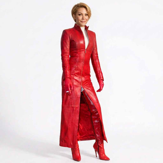A woman modeling a long, glossy red leather coat with a high collar, front zipper, matching red gloves, and red pointed-toe heeled boots against a plain white studio background.