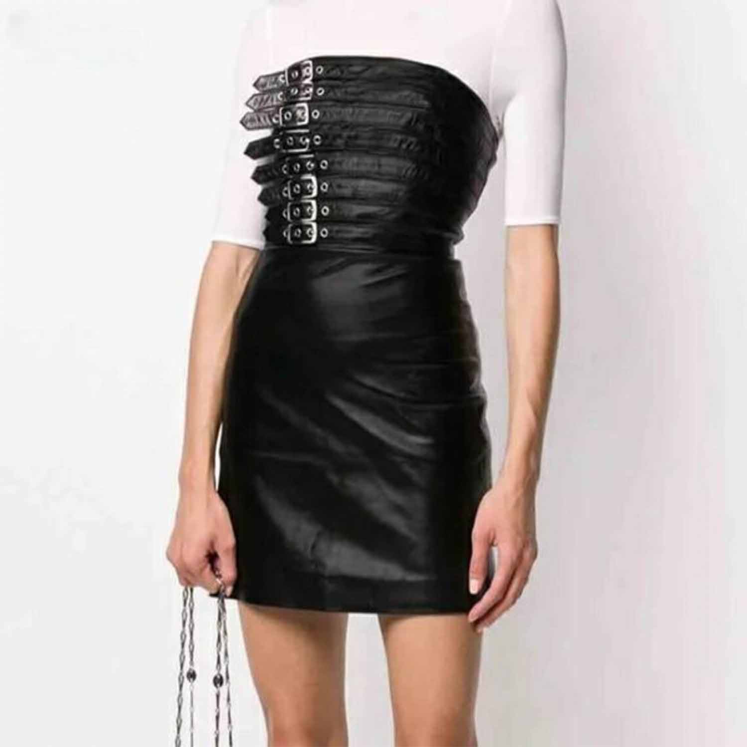 Front perspective of a woman wearing a strapless black lambskin leather buckle mini dress layered over a white long-sleeve top.