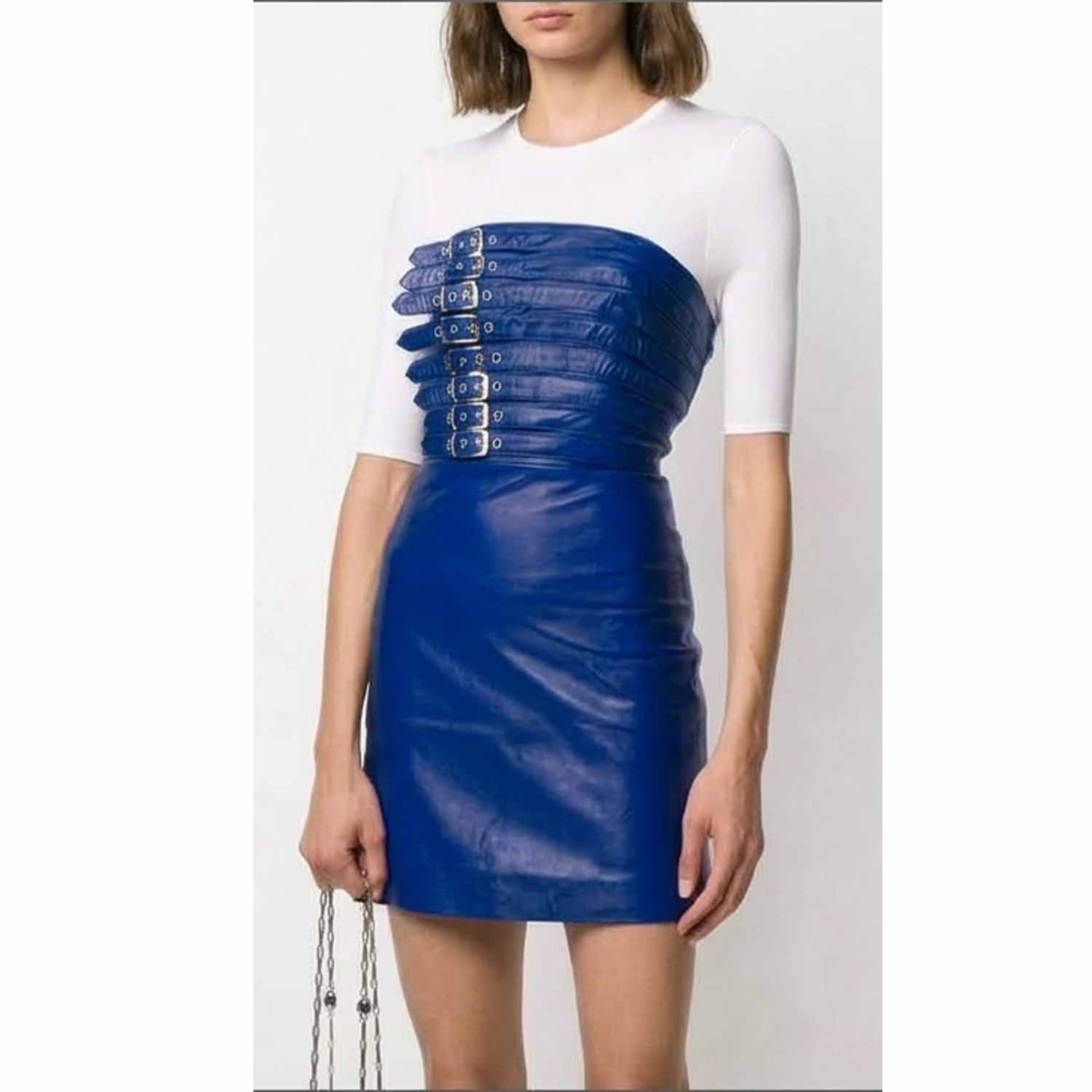 A model wearing a royal blue strapless mini leather dress with a structured corset-style bodice featuring multiple silver-tone buckle details over a white short-sleeve top, set against a plain light gray background.