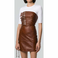 A model wearing a brown leather mini skirt with a structured, strap-belted corset-style waist panel featuring silver-tone metal grommets, paired with a white short-sleeve crewneck top.