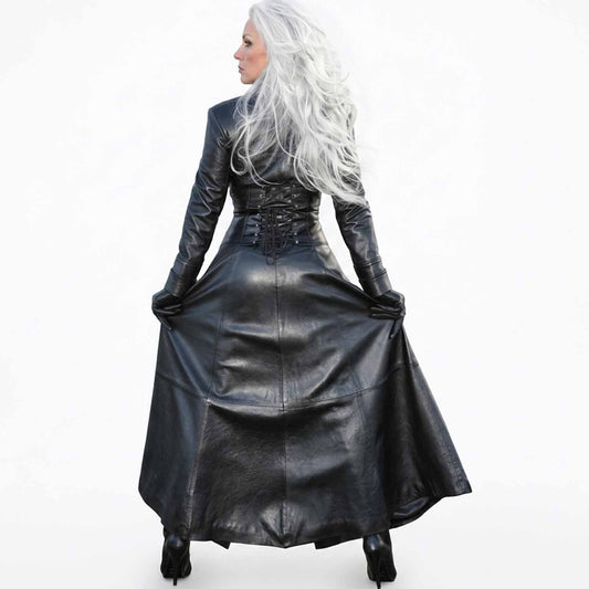 A woman with long white hair is shown from the back wearing a long black leather dress with long sleeves, a lace-up corset-style waist, and a full skirt, photographed against a plain white background.