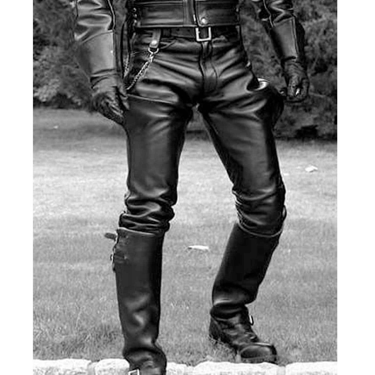 Black leather biker pants with integrated thigh armor and chain details, shown on a model outdoors in a black leather jacket and boots.